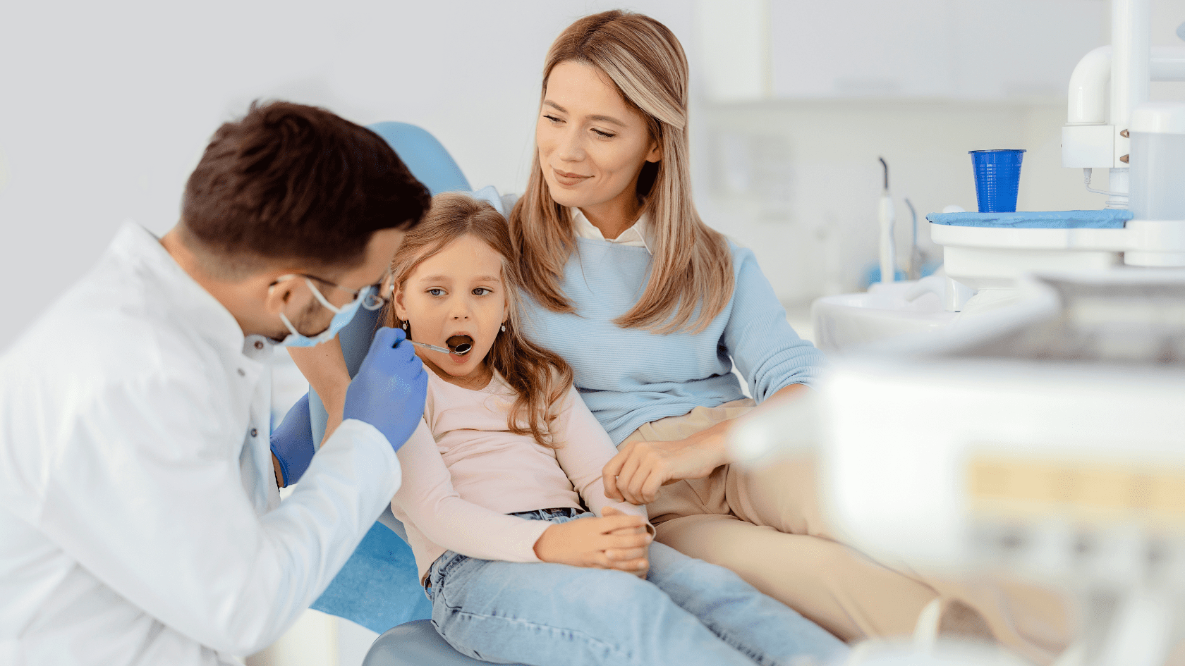 Mom and daughter in a dentist chair while dentist examines the child's teeth.